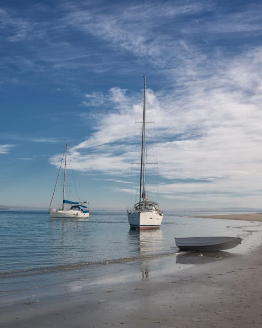 Yachts anchored in the shallows off a Langebaan beach, with a dinghy pulled up on the sand